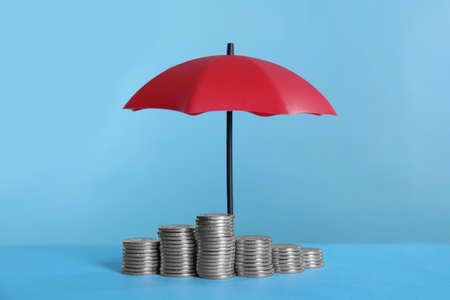 Small umbrella and coins on light blue backgroundの写真素材