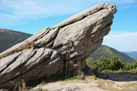 Trekking poles near rock in mountains. Hiking accessory
