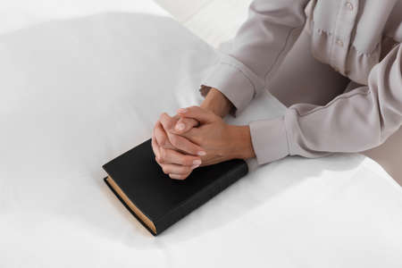 Religious woman with Bible praying in bedroom, closeup