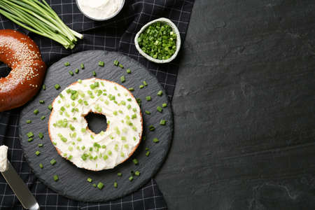 Delicious bagel with cream cheese and green onion on black table, flat lay. Space for textの写真素材
