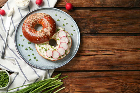 Delicious bagel with cream cheese, green onion and radish on wooden table, flat lay. Space for textの写真素材