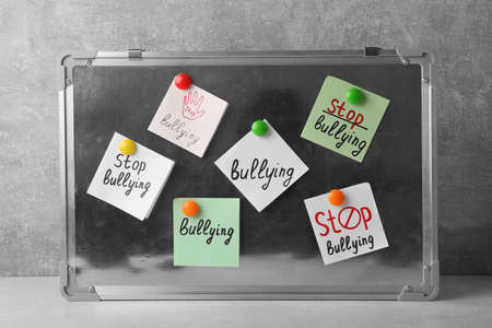 Notes with phrase Stop Bullying attached to board on table near gray wall