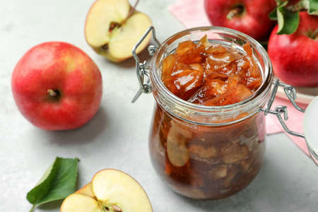 Tasty apple jam in glass jar and fresh fruits on light tableの写真素材