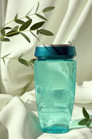 Bottle of hair care cosmetic product and green leaves on light fabric