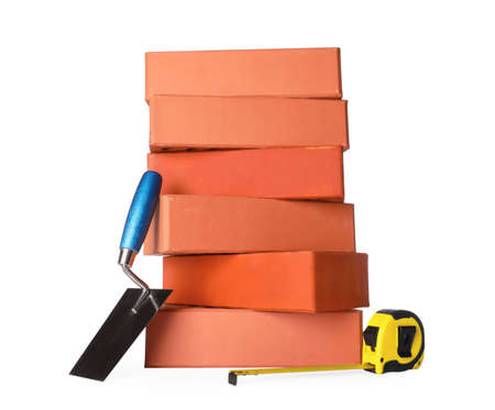 Many red bricks, trowel and tape measure on white background