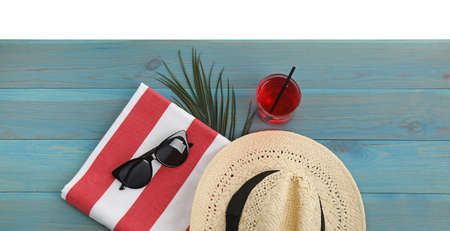 Light blue wooden surface with beach towel, straw hat, refreshing drink and sunglasses on white background, top viewの写真素材