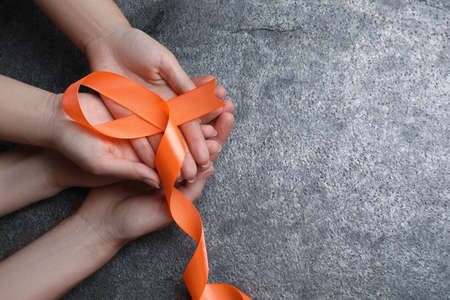 Couple holding orange ribbon on gray background, top view with space for text. Multiple sclerosis awarenessの写真素材