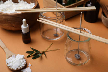 Glass jars with wicks, wax flakes and essential oil on brown background. Making homemade candlesの写真素材