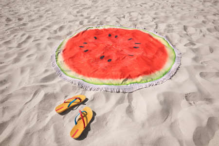 Flip flops and watermelon beach towel with tassels on sandの写真素材
