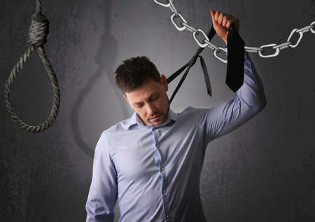 Depressed businessman holding tie like noose against gray background