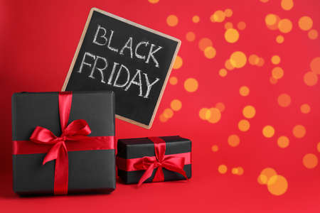 Gift boxes and chalkboard with words Black Friday on red background, space for textの写真素材