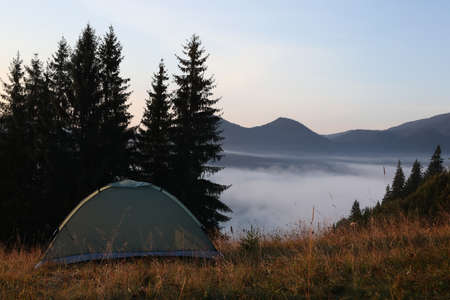 Camping tent in forest clearing near foggy mountains. Space for textの写真素材