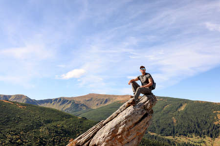 Man with backpack on rocky peak in mountains. Space for textの写真素材