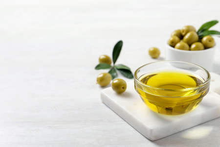 Glass bowl with fresh olive oil on white wooden table, space for textの写真素材