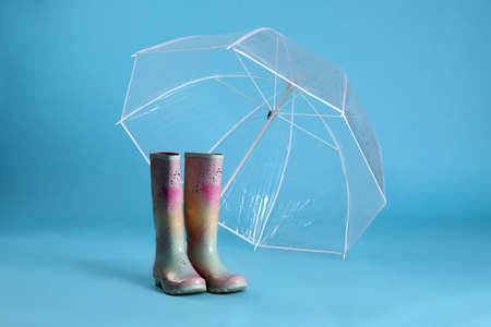 Open transparent umbrella and rubber boots on light blue backgroundの写真素材
