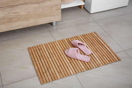 Wooden mat with slippers on floor in bathroomの写真素材