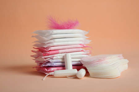 Menstrual pads with pink feather and other period products on pale orange backgroundの写真素材