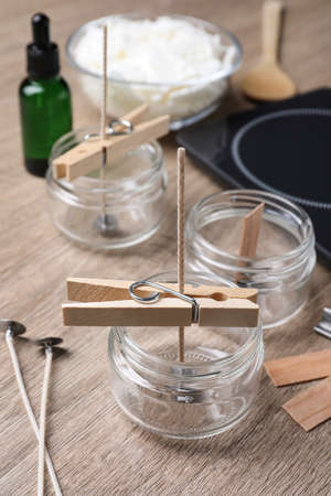 Glass jars with wicks and clothespins as stabilizers on wooden table. Making homemade candlesの写真素材