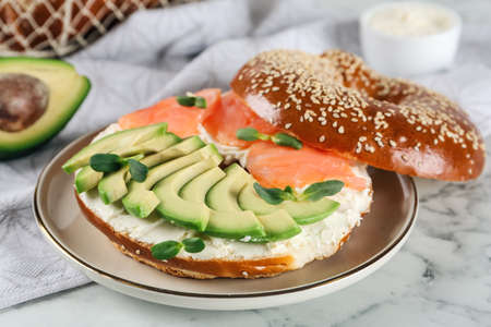 Delicious bagel with cream cheese, salmon, avocado and microgreens on white marble table, closeupの写真素材