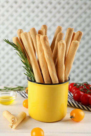 Delicious grissini sticks, rosemary and tomatoes on white wooden tableの写真素材