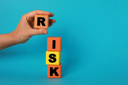 Woman making word Risk with colorful cubes on turquoise background, closeup. Space for text