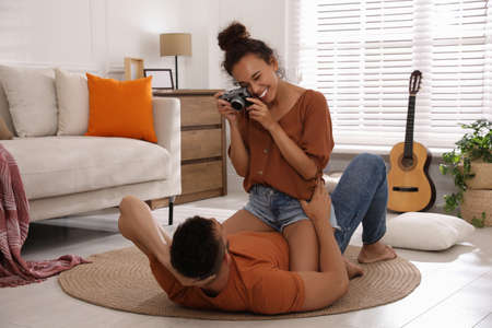 Beautiful African-American woman taking picture of her boyfriend on floor at homeの写真素材