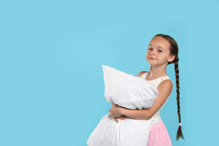 Cute girl wearing pajamas with pillow on light blue background. Space for textの写真素材