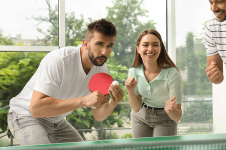 Happy friends playing table tennis together indoorsの写真素材