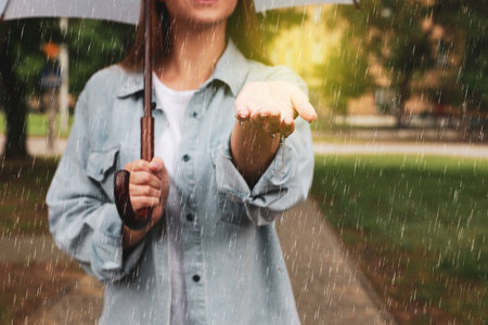 Young woman with umbrella walking under rain in park, closeupの写真素材