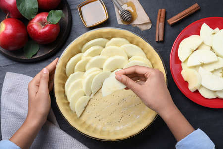 Woman putting apple slices into dish with raw dough at black table, top view. Baking pieの写真素材