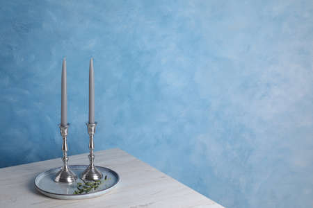 Holders with candles on wooden table near light blue wall, space for textの写真素材