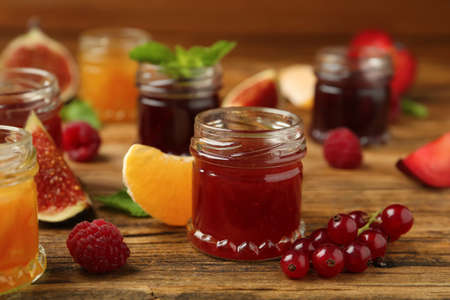 Jars of different jams and fresh ingredients on wooden tableの写真素材