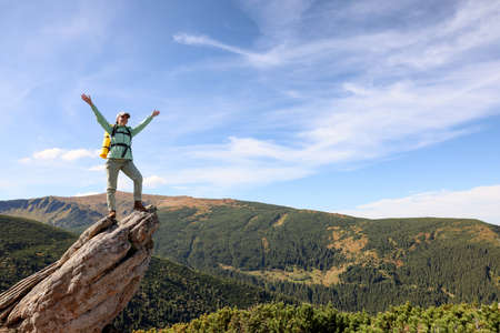 Young woman with backpack on rocky peak in mountains. Space for textの写真素材
