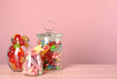 Jars with different delicious candies on pink wooden table, space for textの写真素材