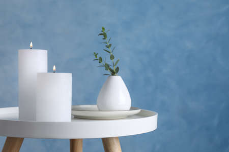 Burning candles and plant on white table against light blue background, space for textの写真素材