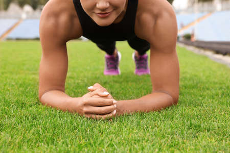 Young woman doing plank exercise on grass at stadium, closeupの写真素材