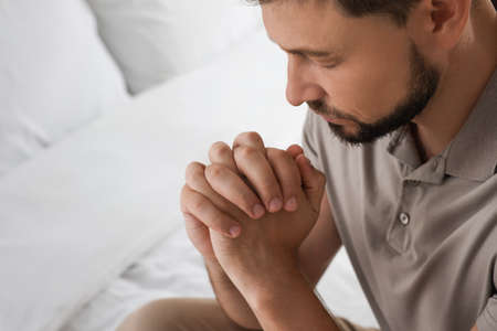 Religious man praying in bedroom, closeup. Space for textの写真素材