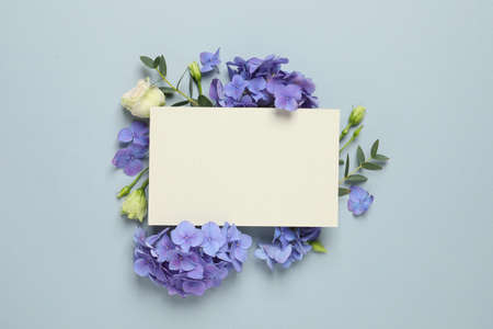 Beautiful composition with hortensia flowers and blank card on dusty light blue background, top view. Space for textの写真素材