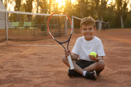 Cute little boy with tennis racket and ball on court outdoorsの写真素材