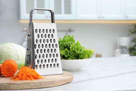 Grater and fresh ripe carrot on white table in kitchen. Space for textの写真素材
