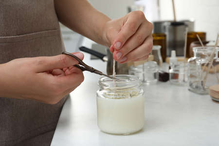 Woman cutting wick of homemade candle at table indoors, closeupの写真素材