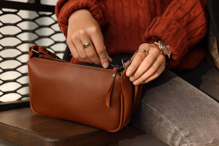 Fashionable woman with stylish bag on bench outdoors, closeupの写真素材