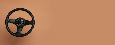 Black steering wheel on light brown background, top view with space for text. Banner designの写真素材