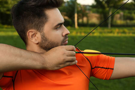 Man with bow and arrow practicing archery in park, closeupの写真素材