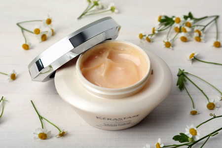 MYKOLAIV, UKRAINE - SEPTEMBER 07, 2021: Kerastase hair care mask and chamomile flowers on white wooden tableのeditorial素材