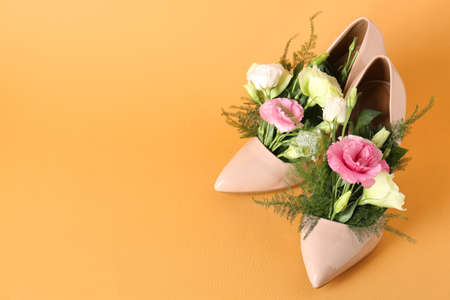 Stylish women's high heeled shoes with beautiful flowers on pale orange background, space for textの写真素材