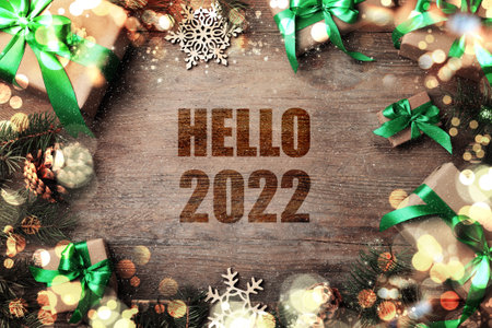 Text Hello 2022, gift boxes and Christmas decorations on wooden table, flat lay