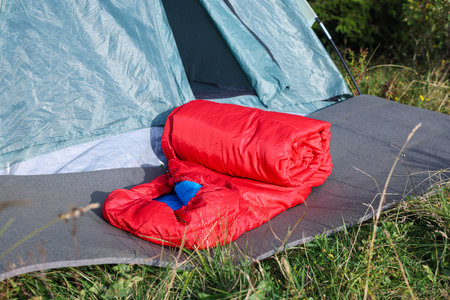 Red sleeping bag near camping tent on green grass outdoorsの写真素材