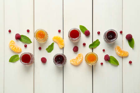 Jars of different jams and fresh ingredients on white wooden table, flat layの写真素材