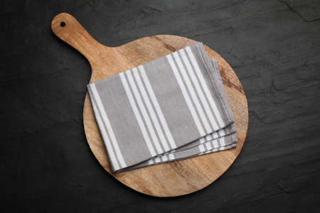 Striped kitchen towel and wooden cutting board on black table, top viewの写真素材